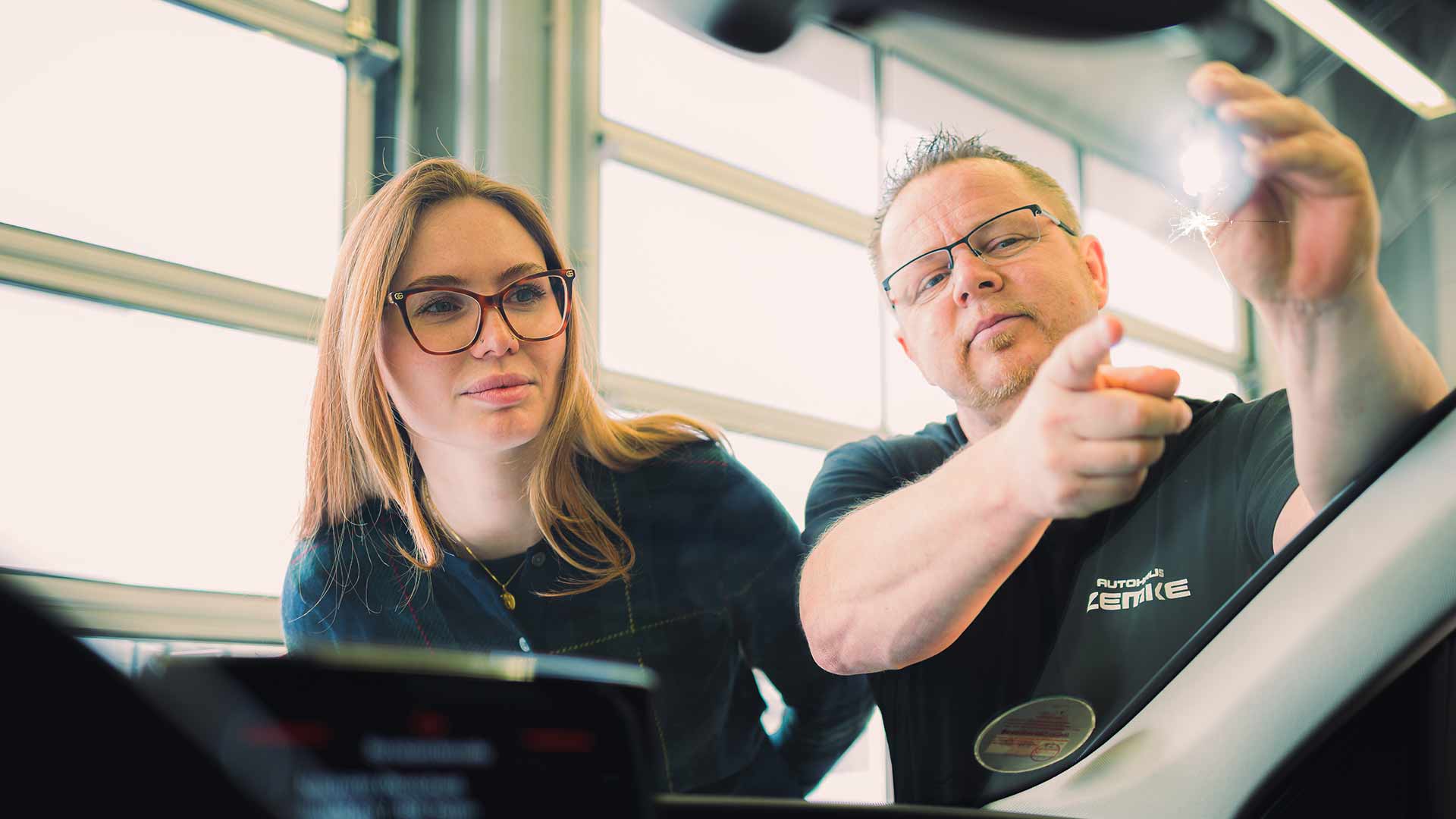 Ein ZEMKE Mitarbeiter zeigt einer jungen Frau einen Steinschlag auf einer Windschutzscheibe