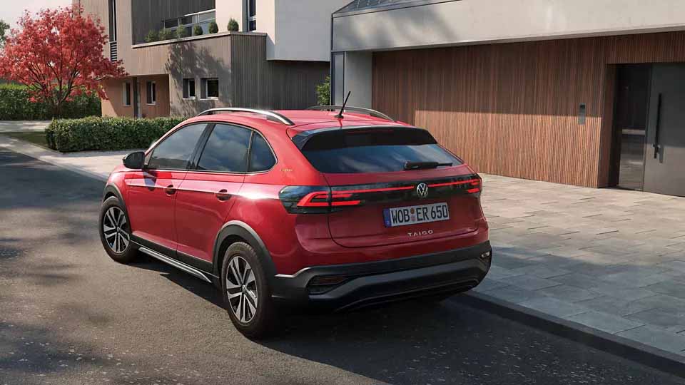 Volkswagen Taigo ENERGY, rot, Heck-Seitenansicht, parkend auf Straße vor Einfamilienhaus