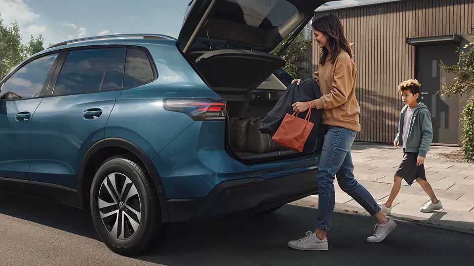 Volkswagen Tiguan ENERGY, blau, Heck-Seitenansicht, junge Frau belädt Kofferraum