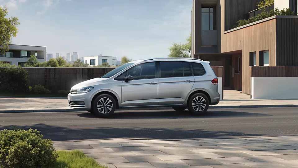 Volkswagen Touran ENERGY, silber, Seitenansicht, parkend auf Straße, moderne Architektur im Hintergrund