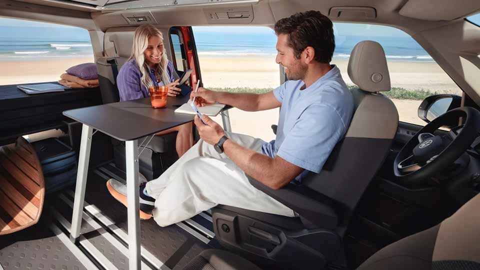 Pärchen sitzt im VW California am Tisch und führt Reisetagebuch